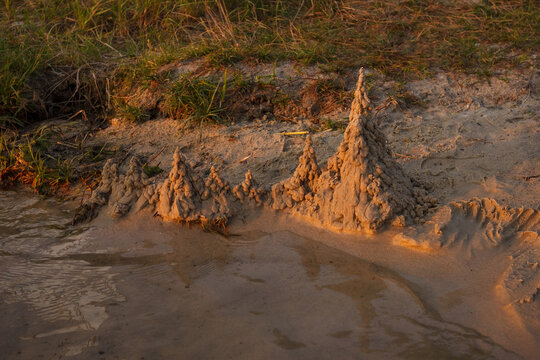 Sand castle on the beach near the water is illuminated by the sunset