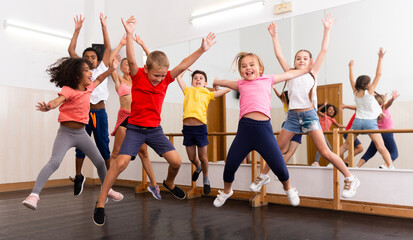 Fototapeta na wymiar Cheerful preteen boys and girls having fun in group dance class, jumping with female coach