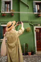 Traveler woman takes photo of color house on Burano island. Girl makes picture on her smartphone 
