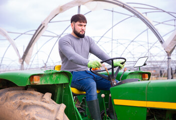 Confident farmer working on tractor in greenhouse. High quality photo