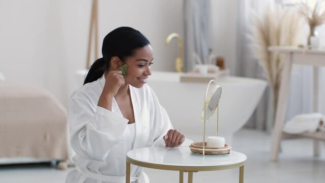 Face building secrets. Young african american lady massaging her face with gouache stone, making anti edema procedures