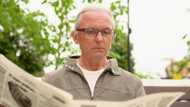 Senior man in glasses reading newspaper in the park. Active retirement