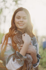 A happy young woman smiles at the camera and holds a young chicken that lays eggs for her farm in the sunlight © SHOTPRIME STUDIO