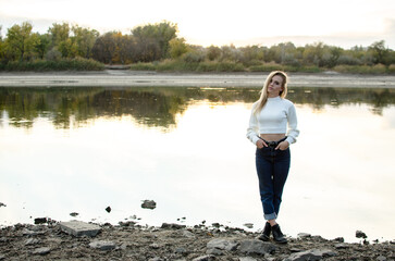 Fototapeta na wymiar Beautiful young woman stands alone on the bank of the river in a white sweater