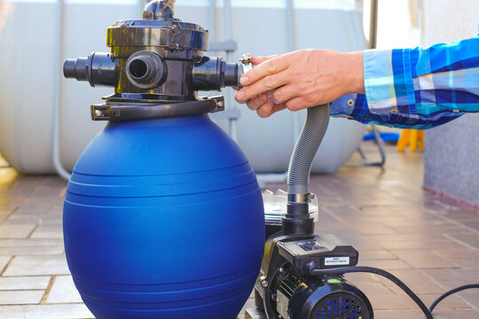  pool cleaning equipment.Blue water filter in the hands of a man in a blue plaid shirt on terrace near the house.man moves the hoses to the filter in the pool close-up.