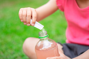 Drink with electrolytes in a transparent bottle in the hands of a happy child on a green lawn in a...