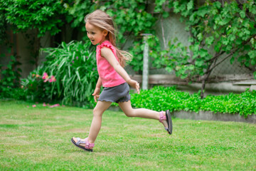 a happy child on a green lawn in a pink T-shirt runs on the lawn