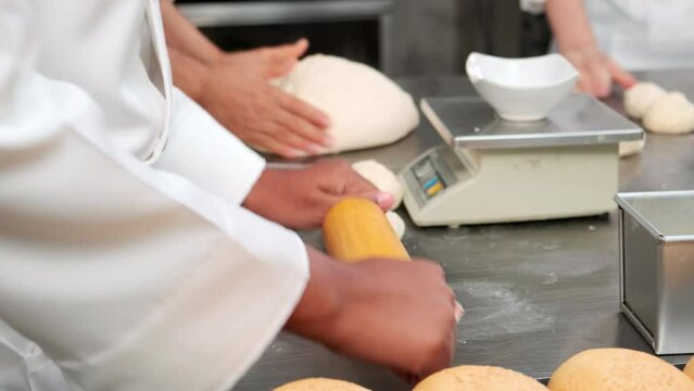 Close up of chefs' hand in white cook uniforms and aprons are kneading raw pastry dough, preparing bread, cakes, cakes, and fresh bakery food, baking in oven at stainless steel kitchen of restaurant.