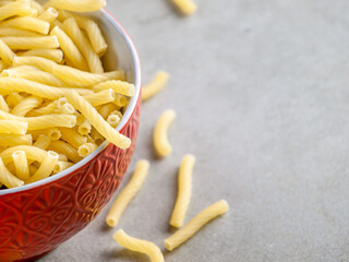 Closeup of Italian food yellow raw uncooked vermicelli, macaroni, noodle, pastry, pasta on the isolated bowl (close-up,meal, cuisine, cooking, gray, dry, dish, studio, plate,dinner, tile, cement)
