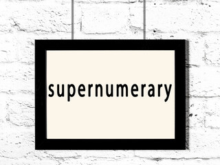 Black frame hanging on white brick wall with inscription supernumerary