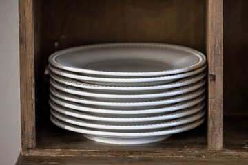 A stack of white porcelain dinner plates in a wood cabinet in a home or restaurant