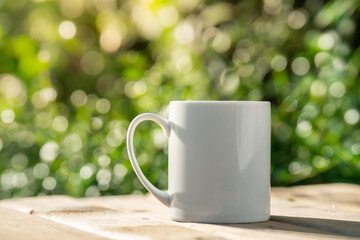 white ceramic coffee mug On the wooden floor, green tree bokeh background.