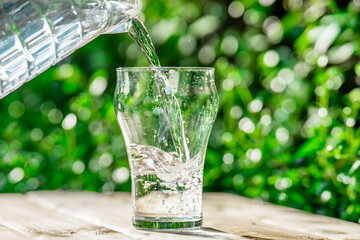 Pour water from a plastic bottle into a glass. The background of the plants in the garden.