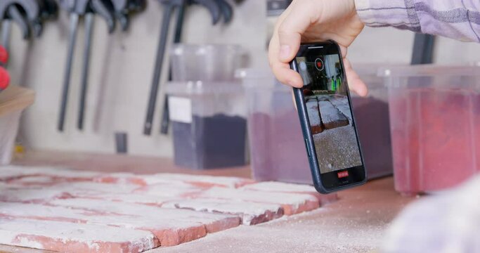 Person is shooting with smartphone worker, who is sweeping away dust from tile imitating brick. Content for construction vlog. Promotional video for online store of finishing decorative materials