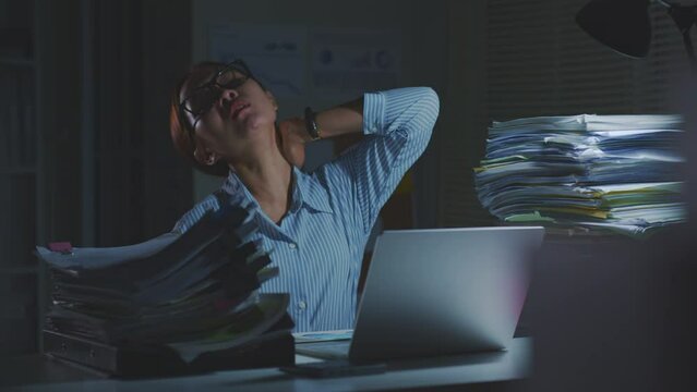 Tired Asian office employee stretching oneself fatigued from using laptop computer for a long time, office syndrome. Working overtime at night