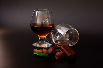 Two glasses of cognac, chocolates, nuts and mint leaves on a black background.