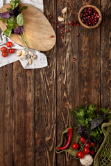 Wooden background with ingredients, fresh greens and textile for food menu. Dark rustic kitchen concept. Empty background in rustic style. Food backdrop with tomatoes, basil, garlic and wooden board.