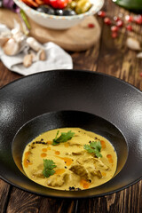 Traditional georgian dish - sacivi with chicken and walnut sauce. Roasted chicken in walnut sauce on black plate. Georgian food on wooden background. Meat appetizer in rustic style on wood table.