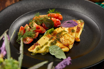 Grilled halloumi cheese with pesto sauce and tomatoes on black plate. Appetizer from fried cheese in greek style on wooden background. Hot appetizer of halloumi cheese in rustic style.