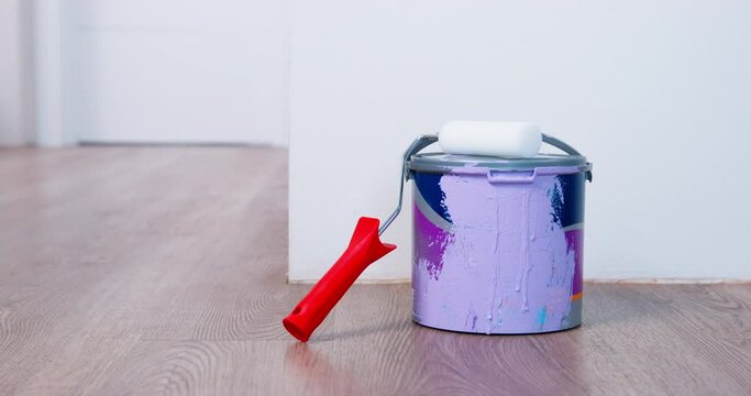 Curvy woman puts roller and bucket with purple paint on wooden floor. Housewife in blue socks brings equipment in room to paint wall closeup