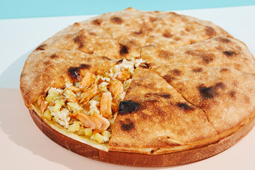 Italian closed pizza with salmon, potatoes and cheese on coloured background. Salmon pie with potatoes and cheese in minimal style. American pizza delivery concept with color backdrop.