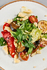 Salad with grilled vegetables, greens and cheese on concrete background. Warm salad with paprika, zucchini, eggplant and tomato on grill. Aesthetic composition with veggie salad. Summer menu concept.