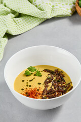 Cream soup with vegetables and crispy meat. Pea cream soup with spices on concrete background. Aesthetic composition with vegetables soup in white ceramic bowl