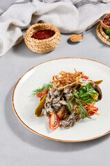 Traditional russian food - beef stroganoff with mashed potatoes and creamy gravy. Beef stroganoff with crispy onion on ceramic plate. Meat ragout with mashed, mushrooms and greens on stone background.