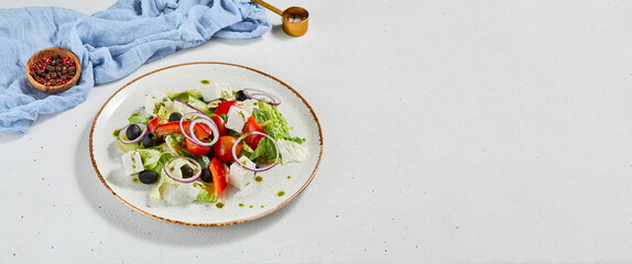 Classic greek salad with pesto sauce on ceramic plate. Vegetable salad with tomatoes, cucumber, paprika, onion and olives. Traditional grecian food. Greek salad on concrete background.