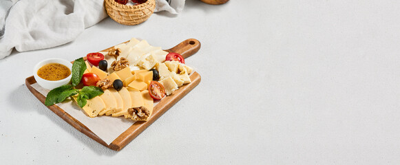 Cheese platter with nuts, honey sauce and olives on wood board. Cheeseboard on white concrete...