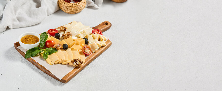 Cheese platter with nuts, honey sauce and olives on wood board. Cheeseboard on white concrete background. Cheese assorted in minimal style. Appetizers for wine.