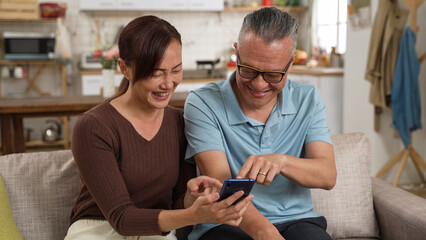 happy asian elderly dad and adult daughter enjoying funny online video on smartphone together in the living room at home.