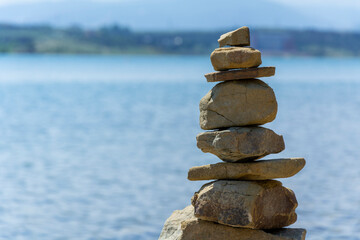 Rock cairn the art of stone balancing on a stone near a blue water flowing lake. Sunny day on the lake. A mood of calm and harmony with nature.