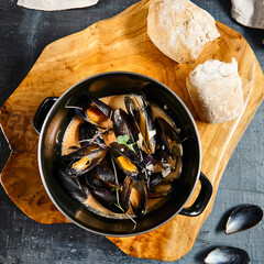 Mussel stew pot with creamy sauce, baguette on stone table. Mussels soup pot contemporary style....