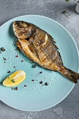 Grilled dorada in blue plate on stone background with textile. Roast fish in restaurant menu concept. Roasted whole dorado with lemon. Contemporary seafood menu. Mediterranean food.
