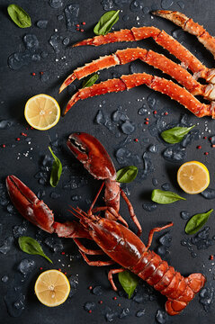 Lobster and crab legs with ice and lemon on dark background top view. Delicatessen crab and lobster seafood on black slate table. Crustacean seafood aesthetics. Luxury food - lobster and crab