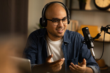 Fototapeta na wymiar Young asian man host streaming podcast with condenser microphone work on laptop at small broadcast home studio. Content creator blogger recording voice over radio interview guest conversation