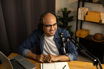 Fototapeta na wymiar Young asian man host streaming podcast with condenser microphone work on laptop at small broadcast home studio. Content creator blogger recording voice over radio interview guest conversation