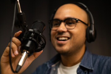 Young asian man host streaming podcast with condenser microphone work on laptop at small broadcast home studio. Content creator blogger recording voice over radio interview guest conversation