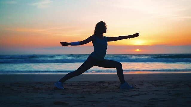 Silhouette Woman practice yoga warrior pose to meditation with summer vacation beach happiness and relaxation. Calm female exercise with yoga meditate ocean beach with sunset. Mental health. 