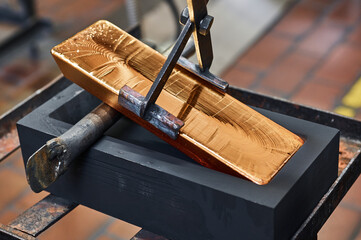 Gold ingot held by tongs in workshop of jewelry plant