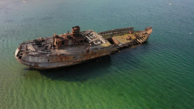 Abandoned wooden hunting schooner Lakhtak built in 1953 in Vityaz Bay. A wrecked wooden ship lies on the seashore, covered with rust. Drone view