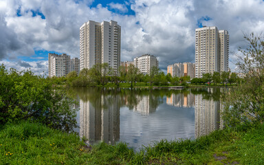 Fototapeta na wymiar In the city park on the shore of the pond high-rise buildings