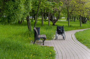 There is a wheelchair on the sidewalk near the bench in the park