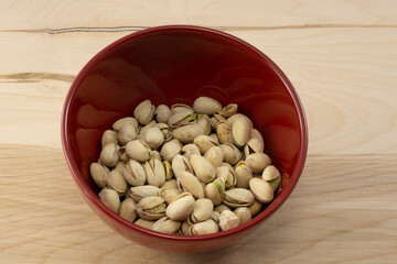 Natural undyed pistachio nuts in red bowl on wooden table