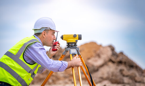 Surveyor engineer wearing safety uniform and helmet with equipment theodolite to measurement positioning on the construction site of the road with construct machinery background