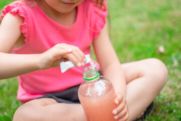 Drink with electrolytes in a transparent bottle in the hands of a happy child on a green lawn in a pink T-shirt