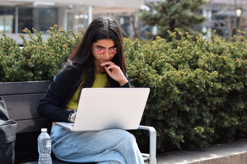 Young girl student sitting on bench working on laptop computer