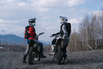 Female motorcyclists wearing helmets sitting on enduro motorbikes turn and looking at camera. Moto...