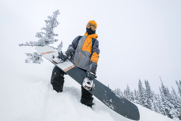 snowboarder holding his board in hands standing on slop in  deep snow